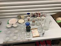 Photo showing assortment of clear glass bowls, ceramic mugs, plates, a glass pitcher, jars, and a poem banner on a table.