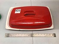 Top view of red-orange lid on white rectangular base with measuring ruler to show width of about 17.5 inches.