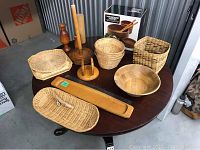 Photo showing full assortment of wicker baskets, wooden bowls, and wooden kitchenware on round dark wood table.