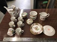 Photo showing all items spread out on table including teapot, cream pitcher, covered sugar bowl, six demitasse cups and saucers, and four small dishes