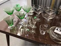 Photo shows an assortment of etched green glass and clear stemware on a table including cocktail glasses, liqueur glasses, and dessert bowls.