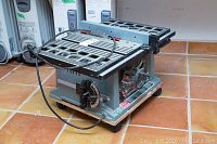 Side angle front view of Delta bench saw showing slotted metal tabletop, power cord, and adjustment mechanisms.