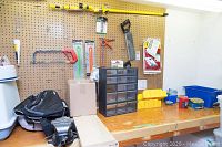 View of workbench with pegboard, showing hand tools (hacksaw, clamps), storage drawers, hardware items, and IKEA shelving planks