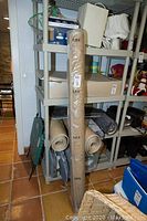 Rolled IKEA Osted rug wrapped in plastic leaning against shelving unit.