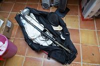 Photo showing black fencing bag containing fencing swords, clothing, and a fencing mask on floor