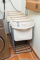 Side view of stacked white IKEA folding chairs showing plastic seats and metal frames