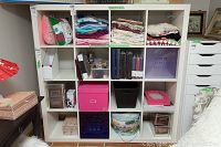 Full view of the IKEA Kallax 4x4 shelving unit filled with assorted storage bins, containers, and fabric materials