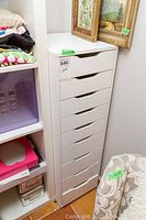 Tall white lingerie drawer cabinet with six drawers and curved cut-out handles in a narrow design. Minor surface wear visible on front edges.