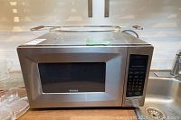 Side view of stainless steel Kenmore microwave on wooden countertop near sink, showing front and side panel.