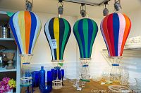 Four colorful handmade fabric hot air balloons displayed on a shelf with blue glass bottles underneath.