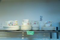 Full set of plates, soup bowls, and teacups displayed on a shelf showing all items in the lot.