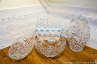 Bohemian crystal vase, fruit bowl, and sectional platters arranged on wooden surface with white tile backsplash. Items display detailed star and pinwheel cut patterns.