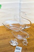 Large swan-shaped clear crystal bowl with long neck and head, shown on wooden surface against tiled white backsplash.