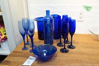 Wide view of the full lot showing 9 cobalt blue flutes, bowl, 12 inch textured bottle, 8 and 9 inch vases grouped together on a wooden surface.