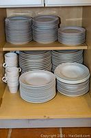 Shelves showing stacked white porcelain dinner plates, luncheon plates, bowls, and mugs.