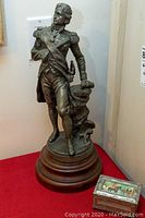 Full view of the Lord Nelson statue on wooden base with the pewter trinket box placed next to it on red fabric.