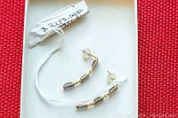 Pair of gold earrings displayed on a white background with a red surface, showing front and side views. Three rectangular blue sapphires aligned vertically per earring with gold settings and posts.