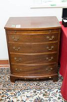 Frontal image of the antique wooden dresser showing four drawers with brass handles and slight bow front shape.