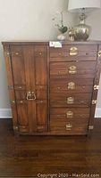 Front view of the wood chest showing six drawers with metal handles and a single cabinet door on the left side with decorative metal latch hardware.
