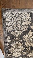 Close-up of the corner edge showing the ornate cream floral damask pattern on dark background and stitched bordering.