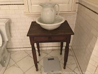 Front view of antique nightstand with porcelain basin and pitcher on top, showing drawer and tapered legs