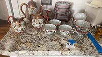Overall view of 10 cups, 10 saucers, 10 dessert plates, teapot, hot water pot, sugar bowl and creamer arranged on countertop