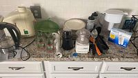 Kitchen countertop showing Hamilton Beach electric glass kettle, Juiceman juicer, drinking glasses with Christmas trees, mini processors, plates, Brita pitcher with filters, and wine rack.