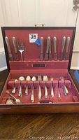 Wooden chest open showing full set of silver flatware on red velvet lining