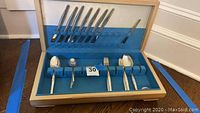 Open wood presentation case with blue interior holding 35-piece flatware arrangement