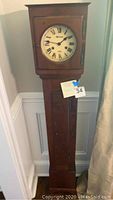 Front view of the wooden baby grandfather clock standing against a wall.