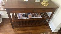 View of the brown wooden foyer table showing the top surface with decorative items and the full table structure including the drawers and slotted shelf.