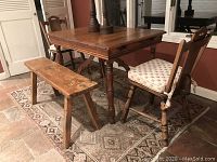 View of the set with table, two panel-back chairs with cushions, and bench on tiled floor with rug beneath.