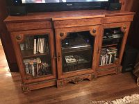 Front view of vintage wooden entertainment credenza showing three glass doors with carved wood surround and brass hardware.