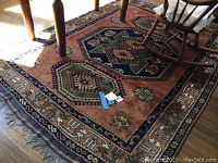 View of large wool area rug under furniture showing central hexagonal design and rust-color background.