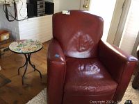 Red leather recliner chair placed next to a round side table with a mosaic tile top and black iron pedestal legs.