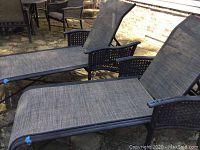 Two chaise lounge chairs side by side on stone patio, showing frames, mesh seating, adjustable backs and wheels