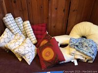 Various pillows including cream with black accents, red Mediterranean style, red chair cushions, body pillow, and two shower curtains.