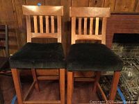 Two upholstered bar stools showing hardwood carved slatted backs, black velvet seat covers, and sturdy wooden frames with footrests.