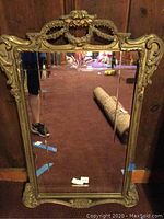 Full front view of the crested carved wood framed mirror standing against a wooden wall.