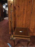 Side view of wooden carved side table with glass top and tall carved giraffe against wood-paneled wall.