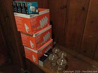 Stack of boxes containing GE 60W light bulbs and flood light bulbs, with four clear glass chandelier covers in front