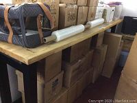 Long view of workshop table with light wood top and black metal frame, boxes stored underneath showing size and sturdy build.