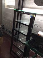 Front angle photo showing six-tier shelf unit with glass shelves and metal rods as accents beneath shelves.