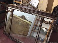 Wide view of the full 3-panel mirror showing dark carved wood frame with gilt highlights, crested top, and side carved jabots.