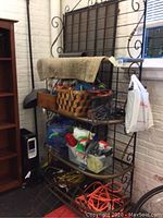 Full view of the vintage wrought iron bakers rack loaded with miscellaneous items showing its overall height and scrollwork detail.