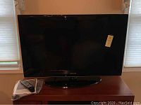 Samsung 40 inch black LCD TV on wooden surface with remote and manual nearby