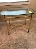 Front view of the side table showing curved glass top and brass frame resting on carpet.