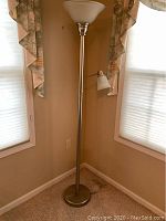 Full view of a brushed nickel floor lamp with torchiere and adjustable reading light in a corner.