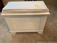 Photo front view of white storage bench showing louvered front and white padded seat.
