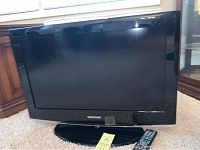 Front view of the Samsung 26 inch television with remote placed on carpet.